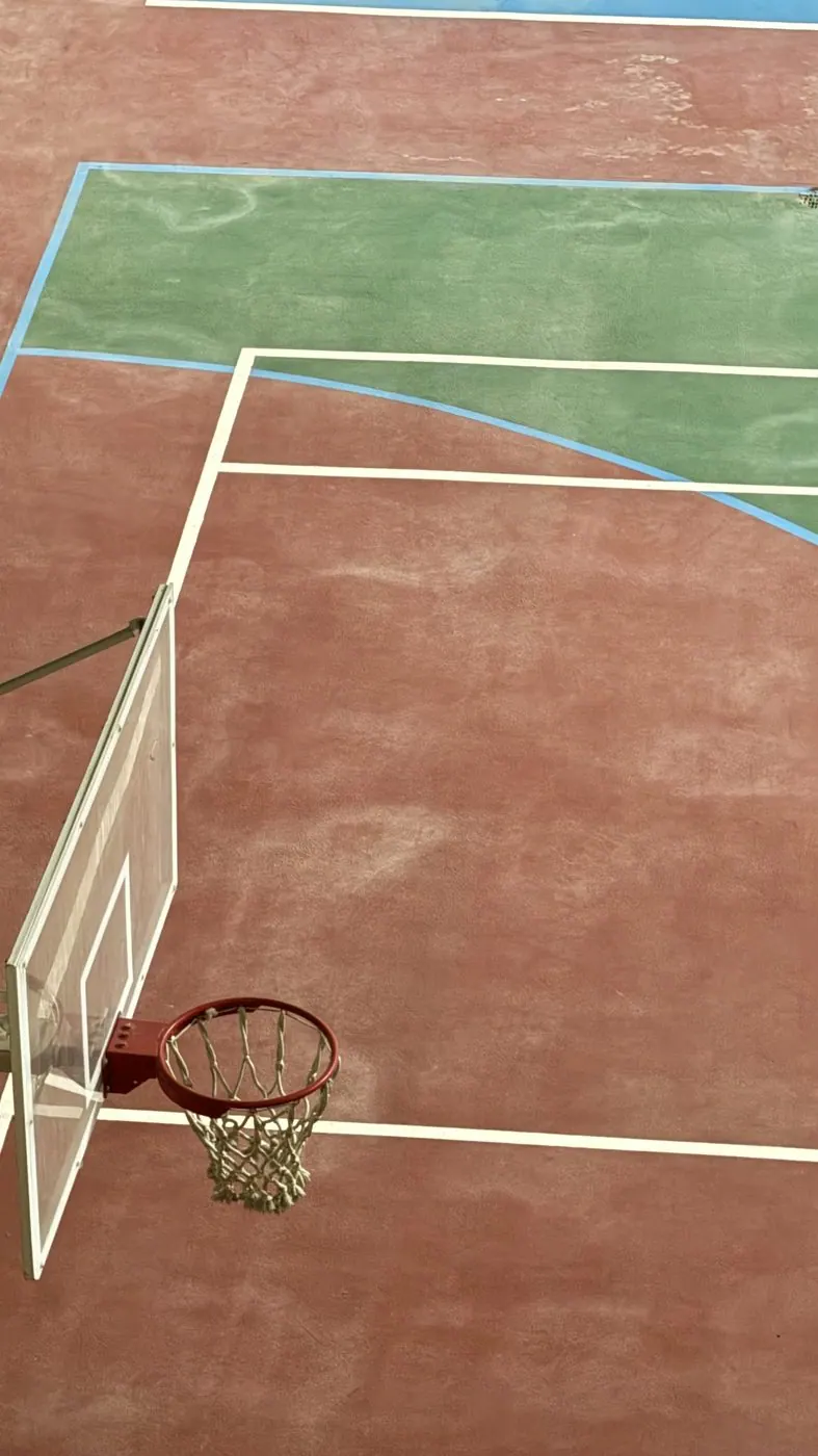 An empty basketball court seen from above, red court and green backboard